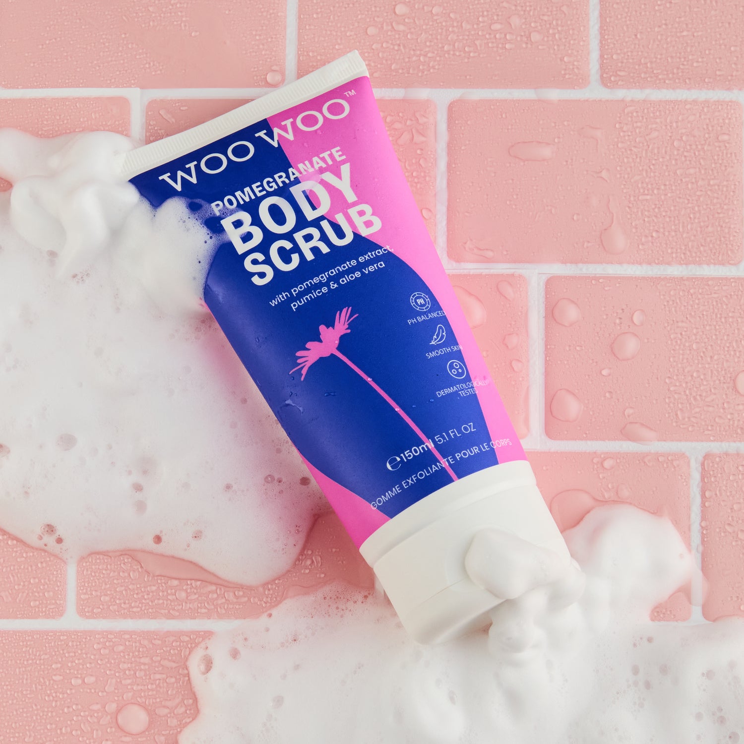 Woo Woo Pomegranate Body Scrub tube with foam on a pink tiled background