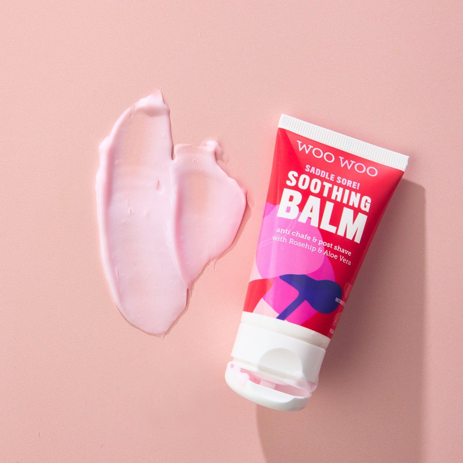 Woo Woo soothing balm tube with pink balm smear on a beige background